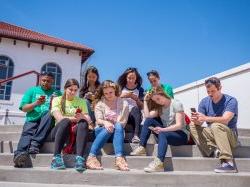 Students sitting on the steps on their phones.
